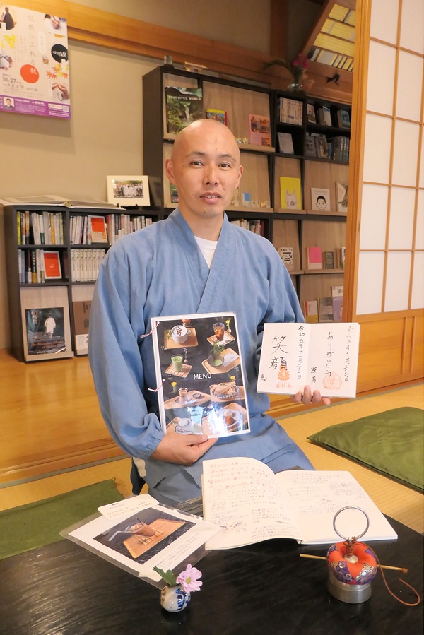 カラフルなメニューと来客が書き込んだ御朱印帳を手にする小野住職